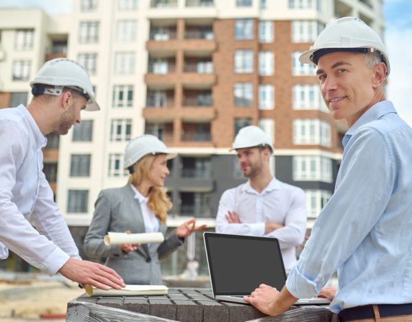 Smiling contented middle-aged engineer posing for the camera with his colleagues on the background